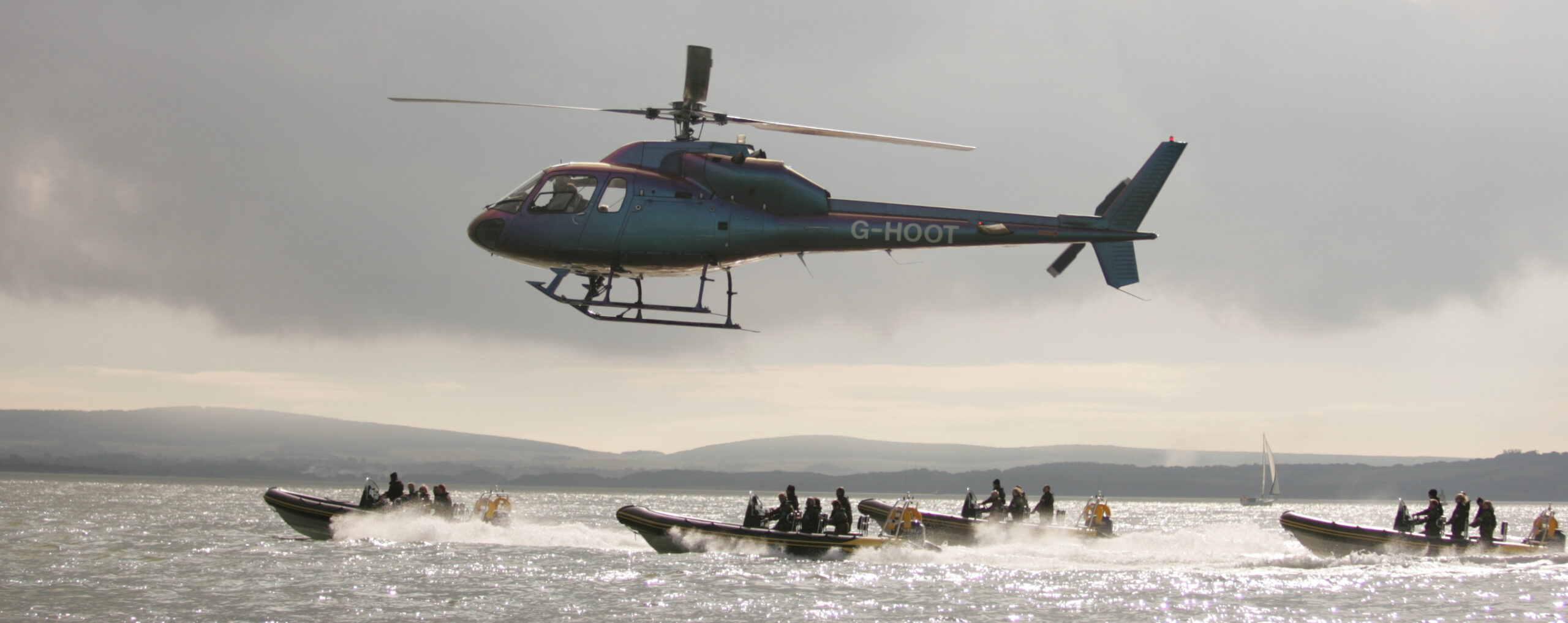 Helicopter flying above a fleet of RIBs during a high-energy corporate adventure event on the Solent