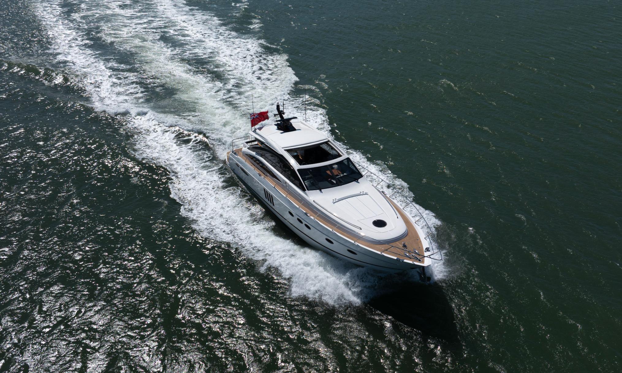 Aerial front view of Princess V65 Varka luxury motor yacht cruising at speed with wake across open water for private yacht charter with Solent Events